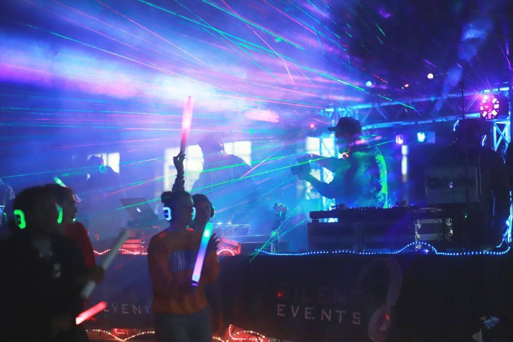 Silhouettes of people dancing in the dark with noise-cancelling LED headphones on and disco lights